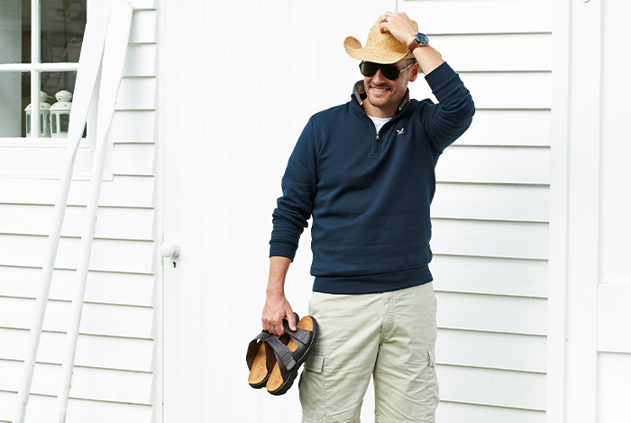 A man holding a pair of sandals in his hands wearing a hat