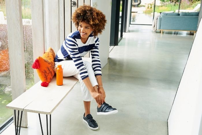 A woman sat on a bench putting on blue shoes