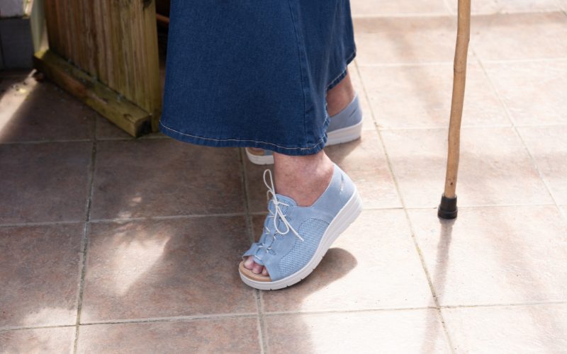 Someone wearing blue sandals, denim skirt, and holding a walking stick