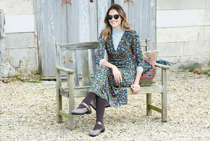 A woman sat on a wooden bench in floral dress