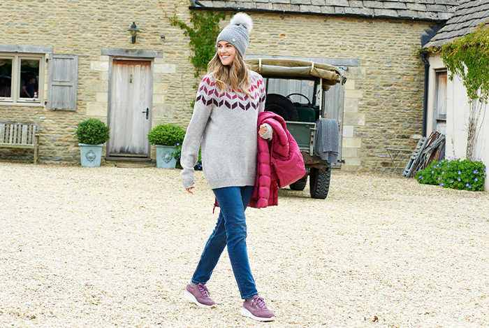 A woman walking carrying a coat and wearing a bobble hat