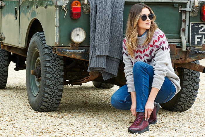 A woman crouching down tying up a lace behind a jeep