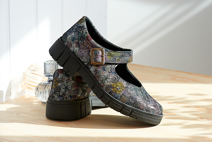 A pair of multi colour foral and black buckle shoes on a wooden table