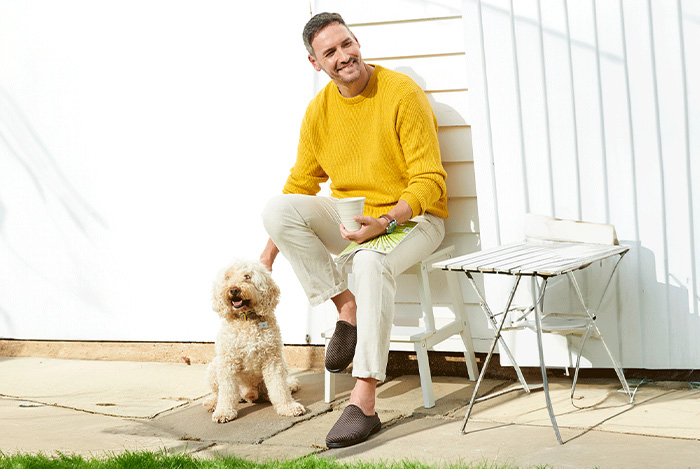 A man sat on a chair in a yellow jumper with a dog by his side