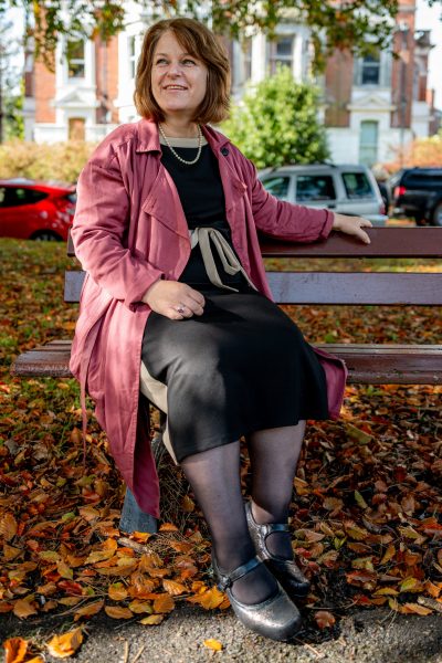 A woman sat on a park bench in black dress and red coat