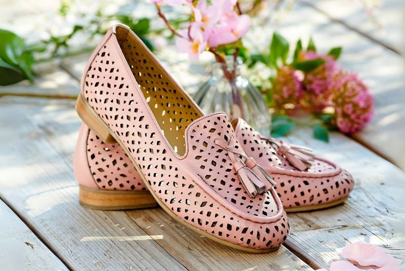 A pair of pink raffia style flat shoes on a wooden table next to flowers