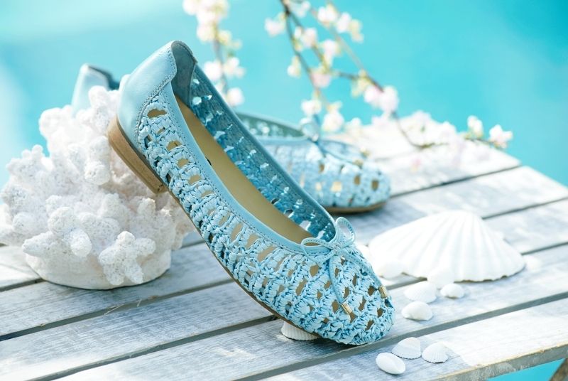 A pair of blue raffia style flat shoes on a wooden table next to a pool
