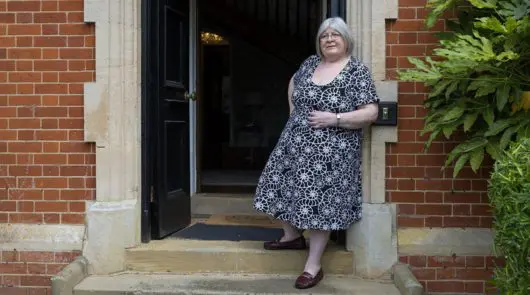 A woman standing in a doorway wearing a blue patterned dress